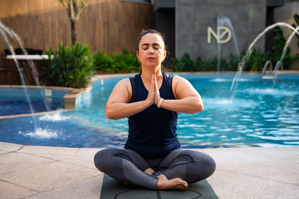 Pessoa meditando perto da piscina no hotel nadai