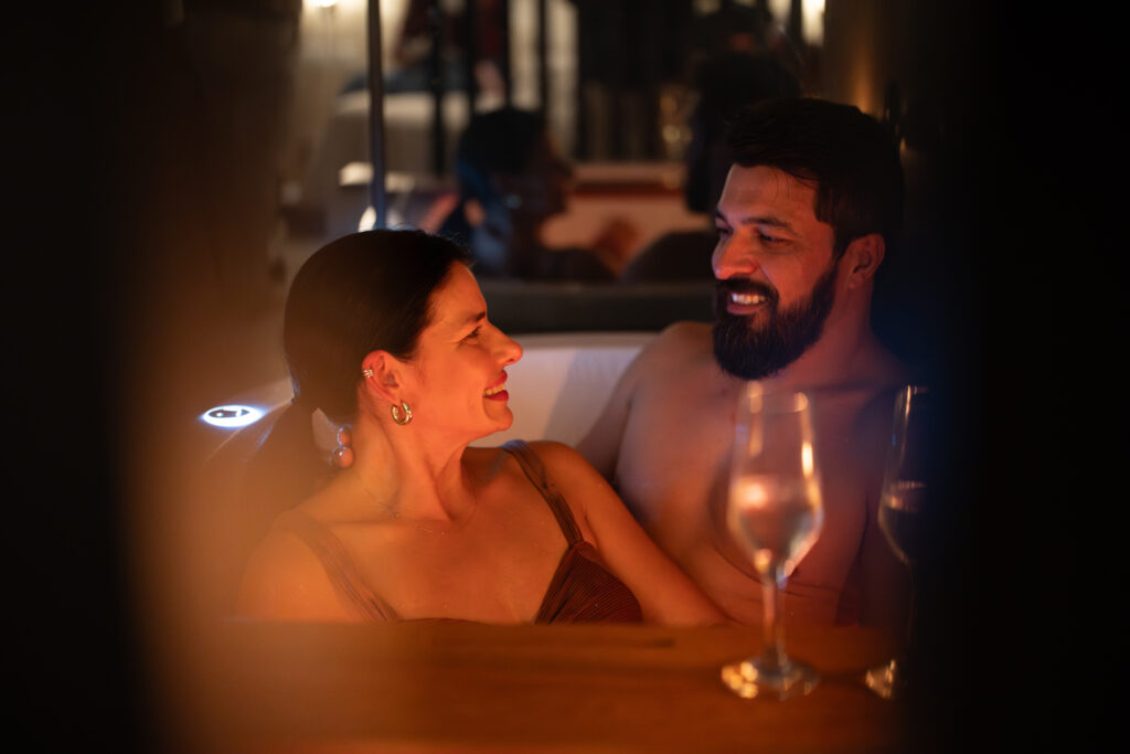 casal aproveitando um banho de ofurô com espumante e luz de velas.