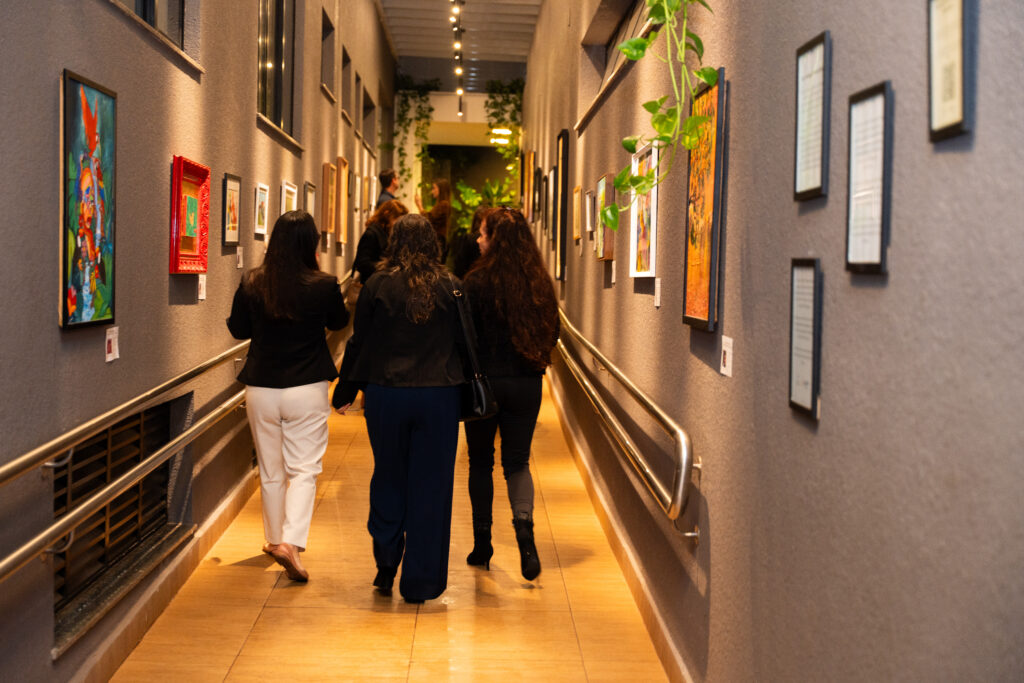 Hotel Nadai em celebra 45 anos com lançamento do Ateliê Nadai by Nair e da exposição Almas do Iguaçu 3 Pessoas caminhando em corredor artístico da exposição almas do Iguaçu, do hotel Nadai em Foz do Iguaçu.