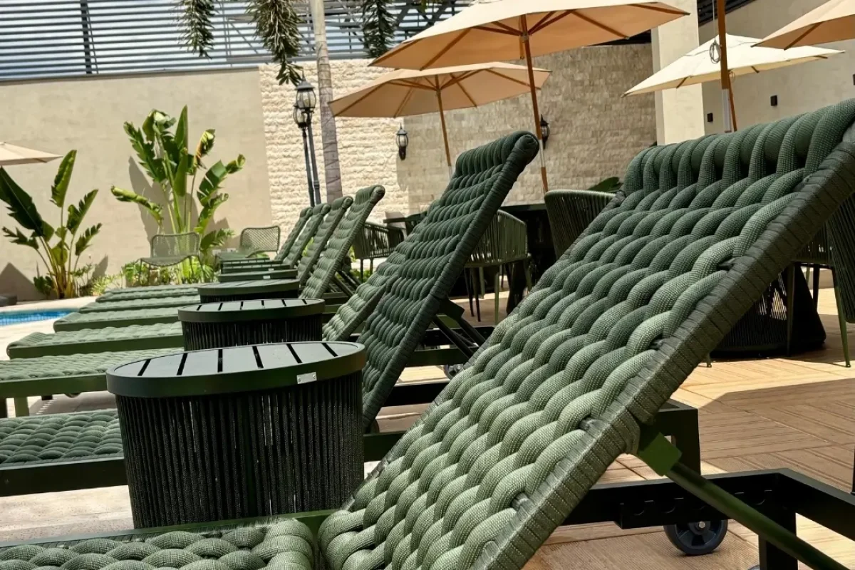Espreguiçadeiras verdes e modernas ao lado da piscina, com palmeira e guarda-sóis.